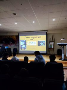 Imagen de un salón de actos donde se ven a los alumnos de espaldas y la imagen del proyector con las diapositivas del taller.